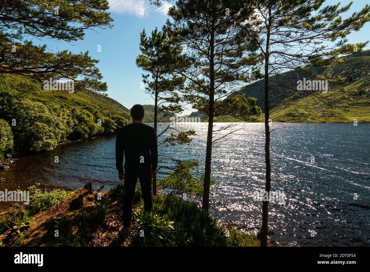 Young man enjoying view of Lough Veagh and rugged Derryveagh Mountains with blue sky in Glenveagh National Park north west of County Donegal, Ireland Stock Photo