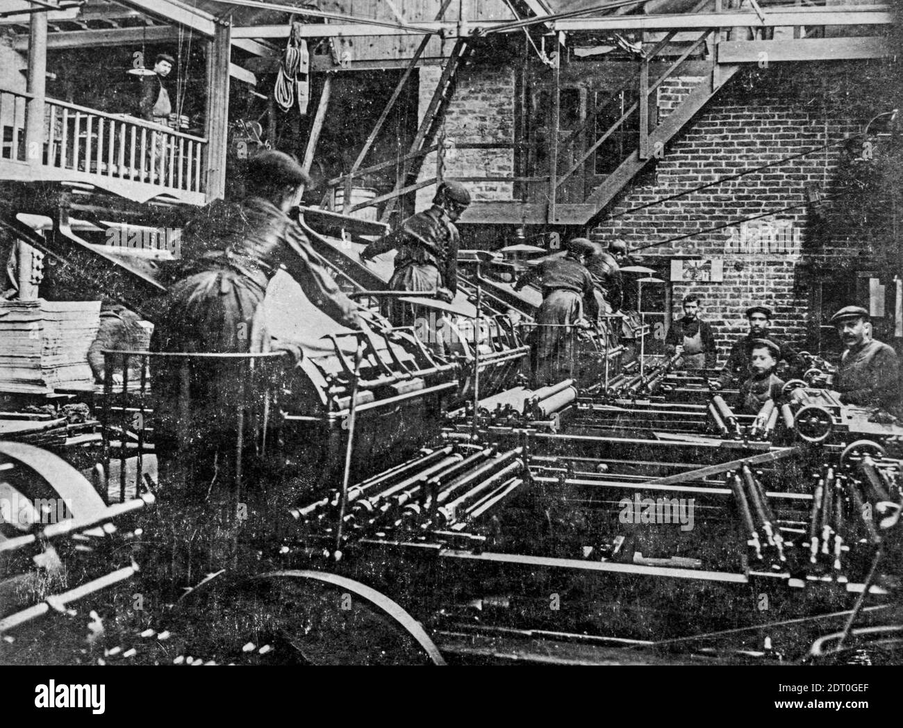 Early 1900s black and white archival photo showing pressmen and children working on lithographic printing presses in pressroom / print shop Stock Photo