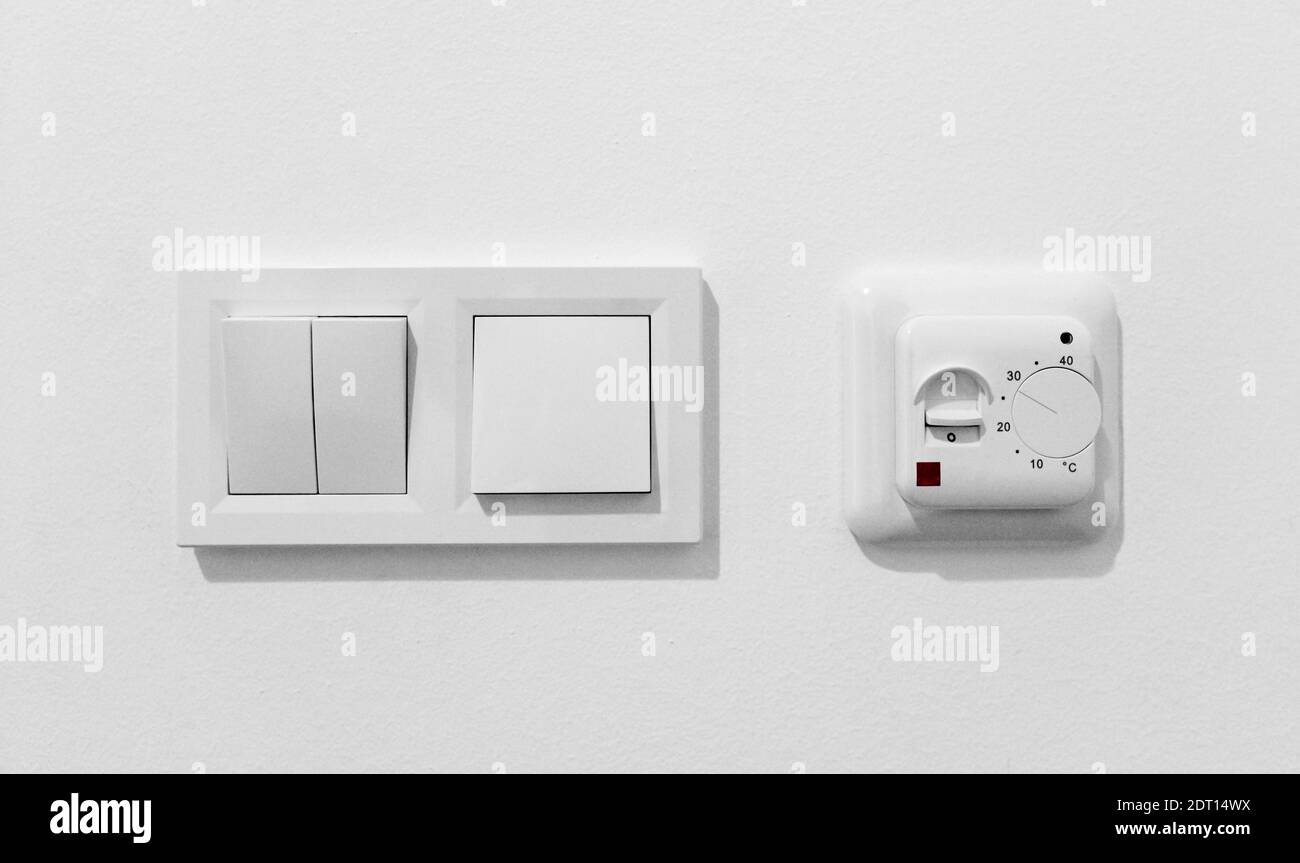 Pair of simple light switches with dimmer. Inexpensive plastic mechanical double switch with thermostat against white wall. Old air conditioner Stock Photo