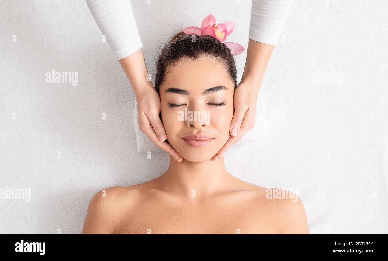 Young asian woman enjoying skin lifting face massage at wellness center Stock Photo