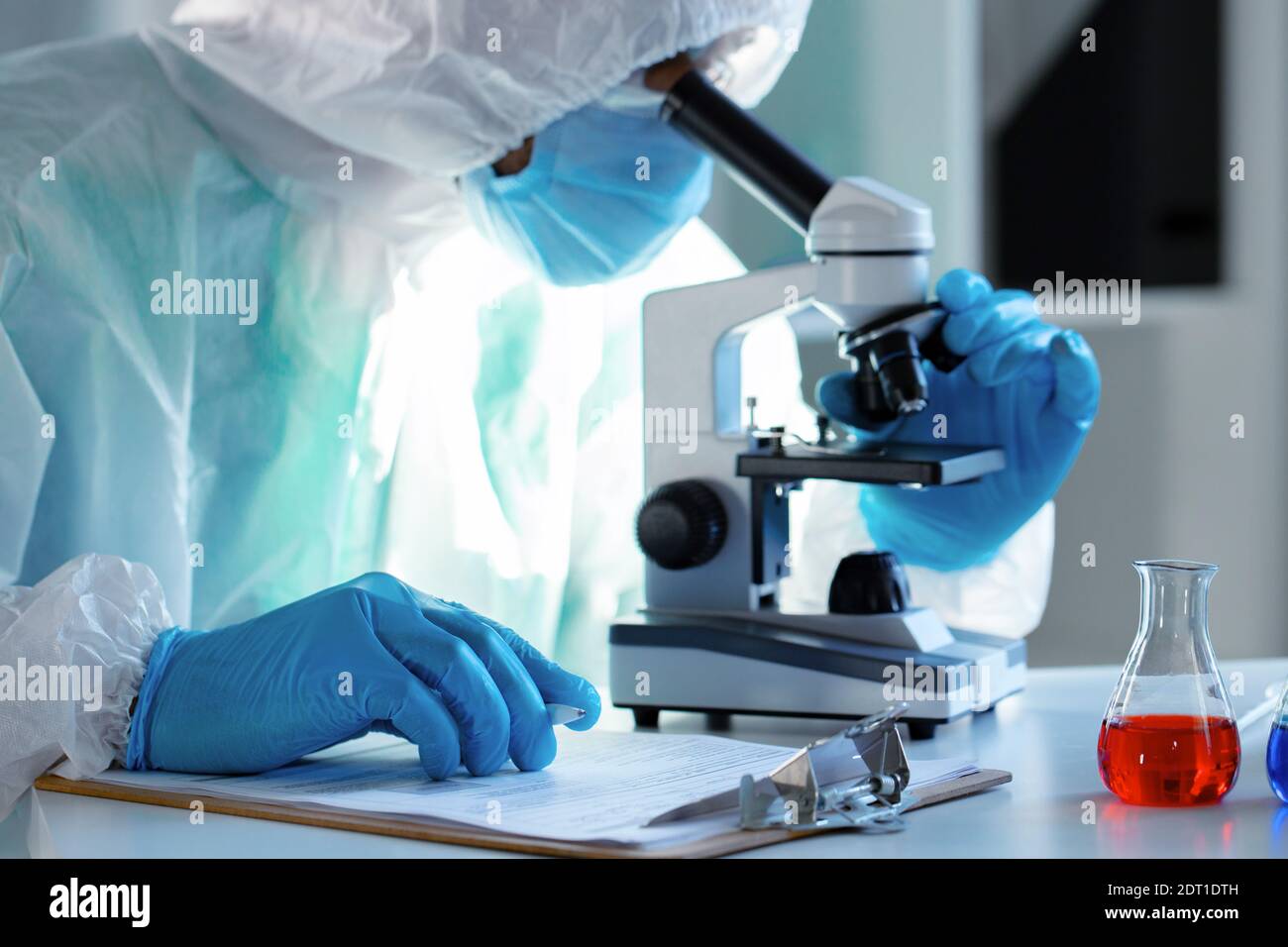 Medical worker in protective gown looking in microscope Stock Photo