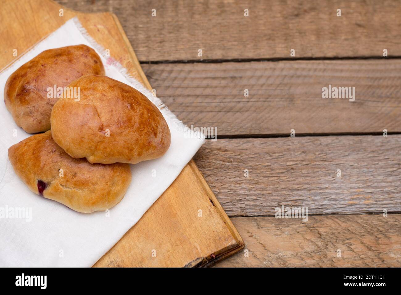 Russian pirozhki (baked patties) with berries on wooden cutboard on wooden background. Stock Photo