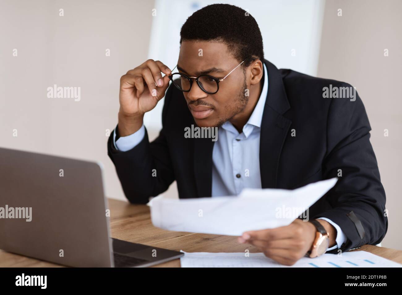 Black guy with glasses accountant holding papers, using laptop Stock Photo