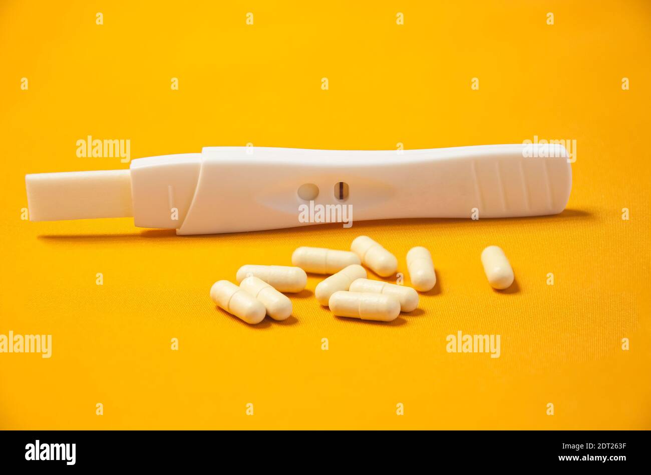 A pregnancy test with a negative result and a handful of birth control pills on a yellow background. Means to prevent pregnancy Stock Photo