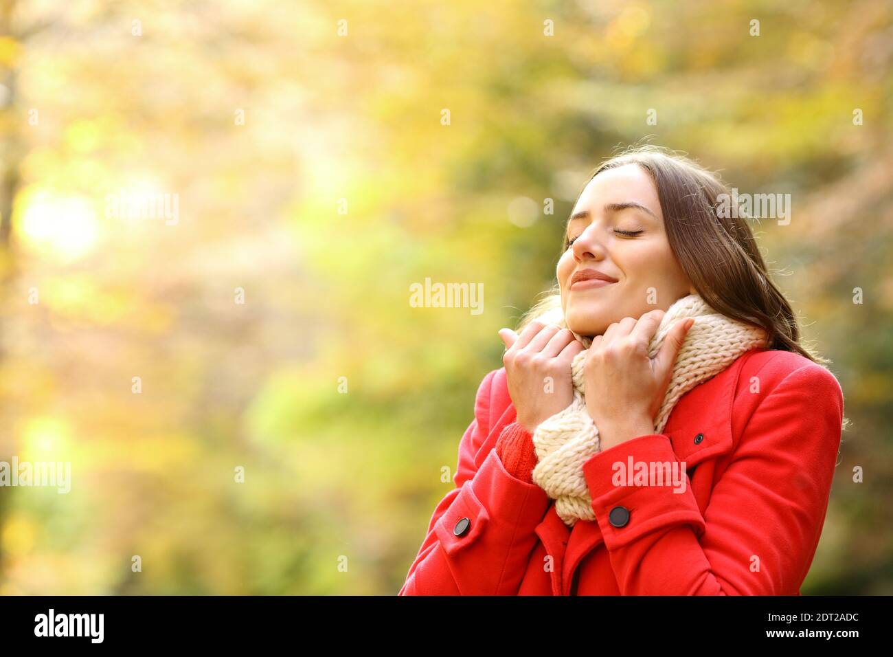 Beauty woman in red jacket heating grabbing scarf in a park in autumn Stock Photo