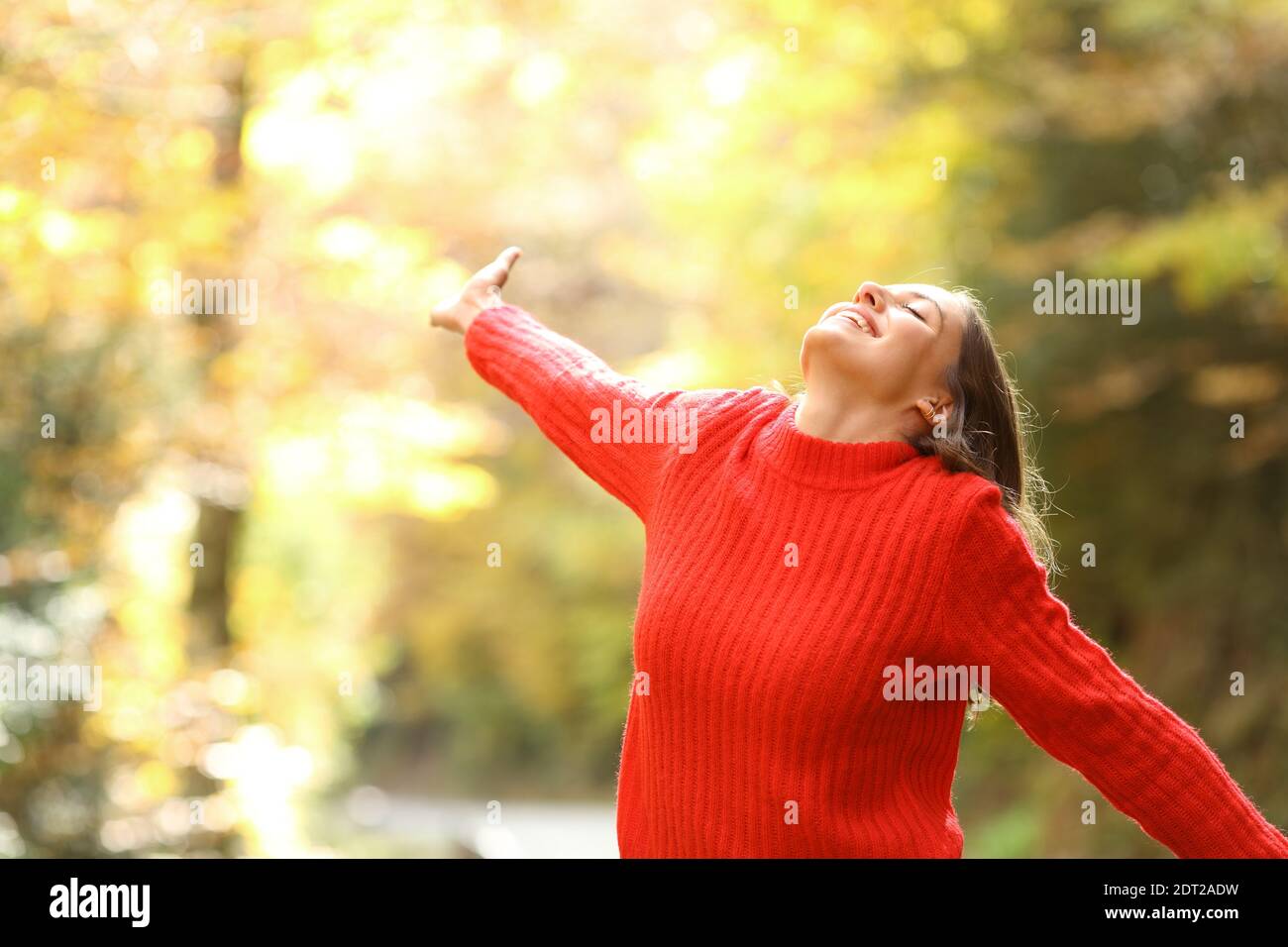 Excited woman in red celebrating vacation standing in a forest in autumn Stock Photo