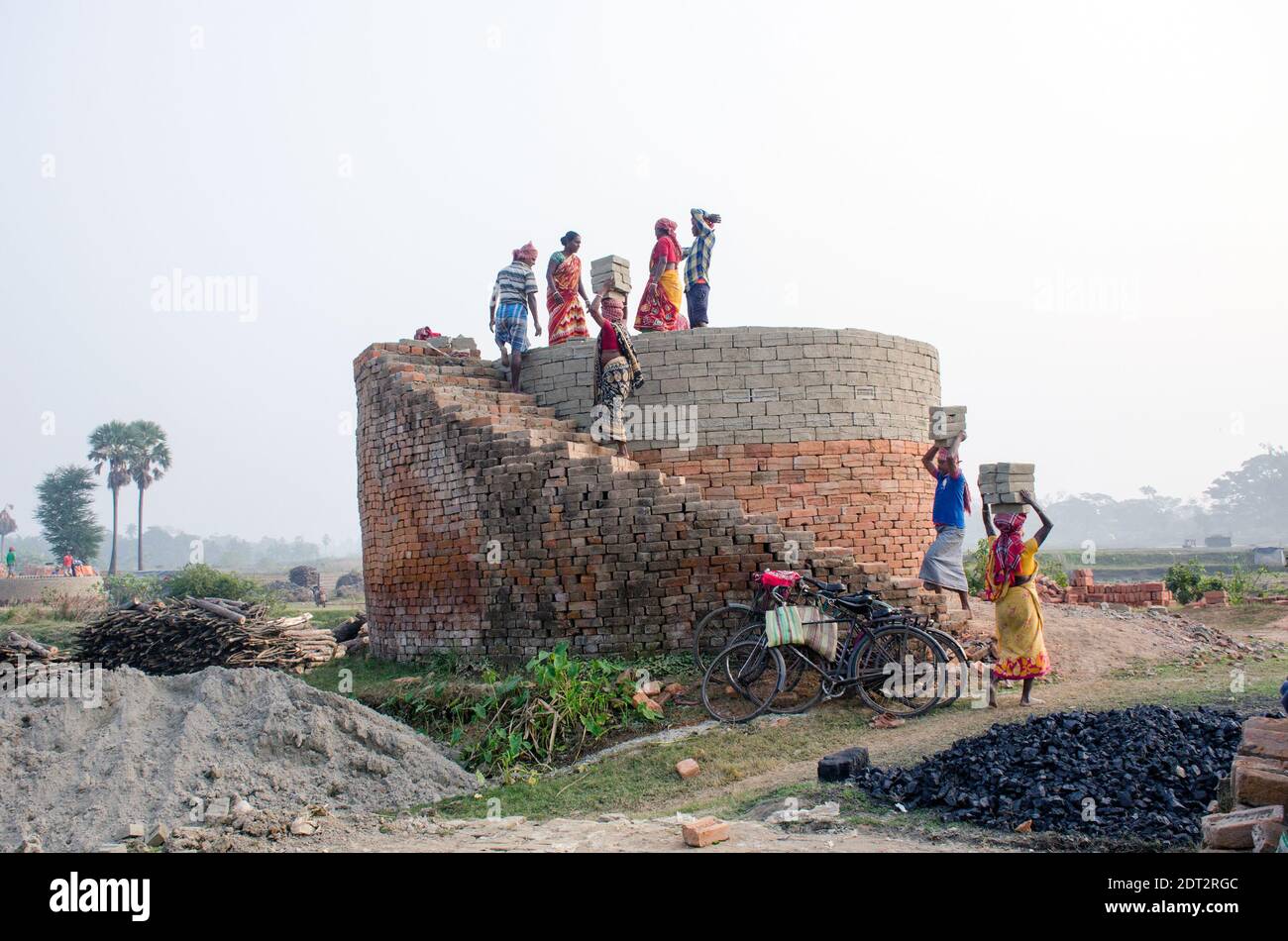 Picture of a brick kiln in the remote Hooghly district. Adult male and female workers work hard to arrange the raw bricks in the kiln to be baked. Stock Photo