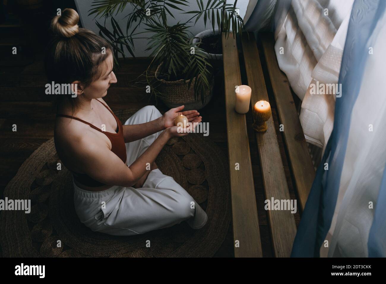 Young woman sitting on the floor, lights candles, enjoy meditation, do yoga exercise at home. Mental health, self care, No stress, healthy habit Stock Photo