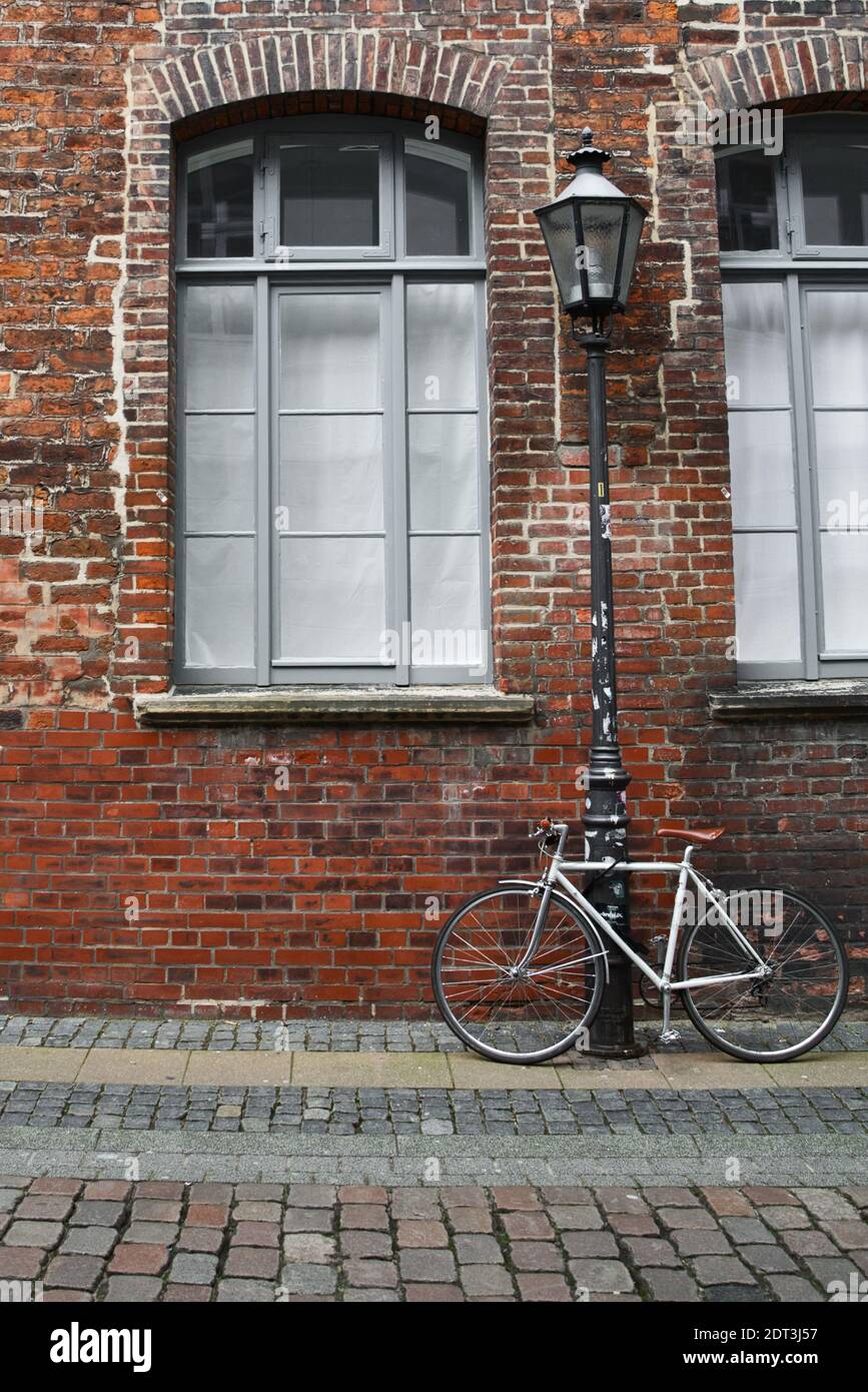 White bicycle tied to a streetlamp in front of a brick wall Stock Photo