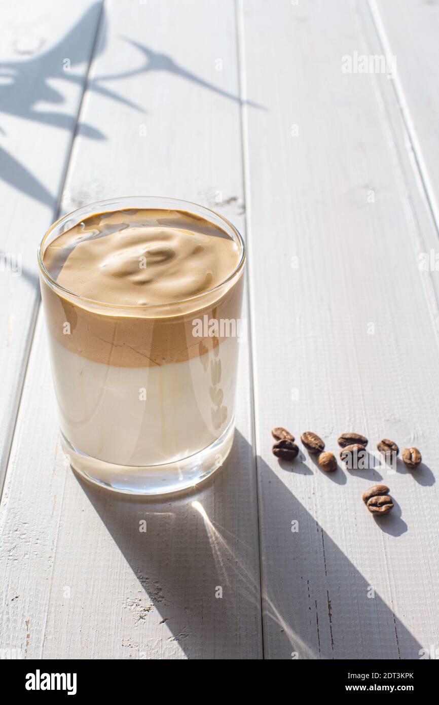 Traditional Korean drink, Dalgona coffee in a transparent glass with coffee beans on a background of white boards. Stock Photo