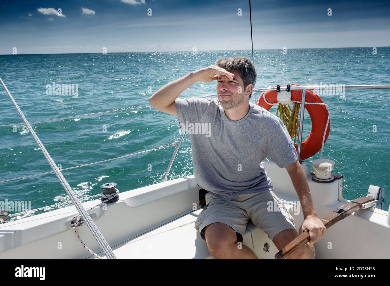 Young man in his late 20's riding a sailboat and looking over the sea for direction. Stock Photo