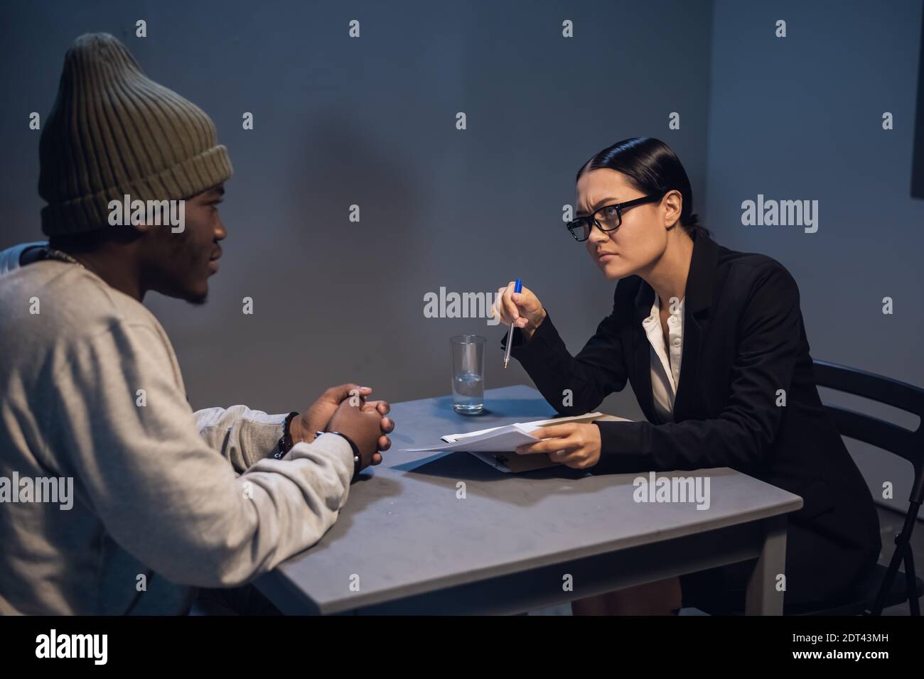 A young girl lawyer consults her client at the police station, a black guy in a cap and handcuffs Stock Photo