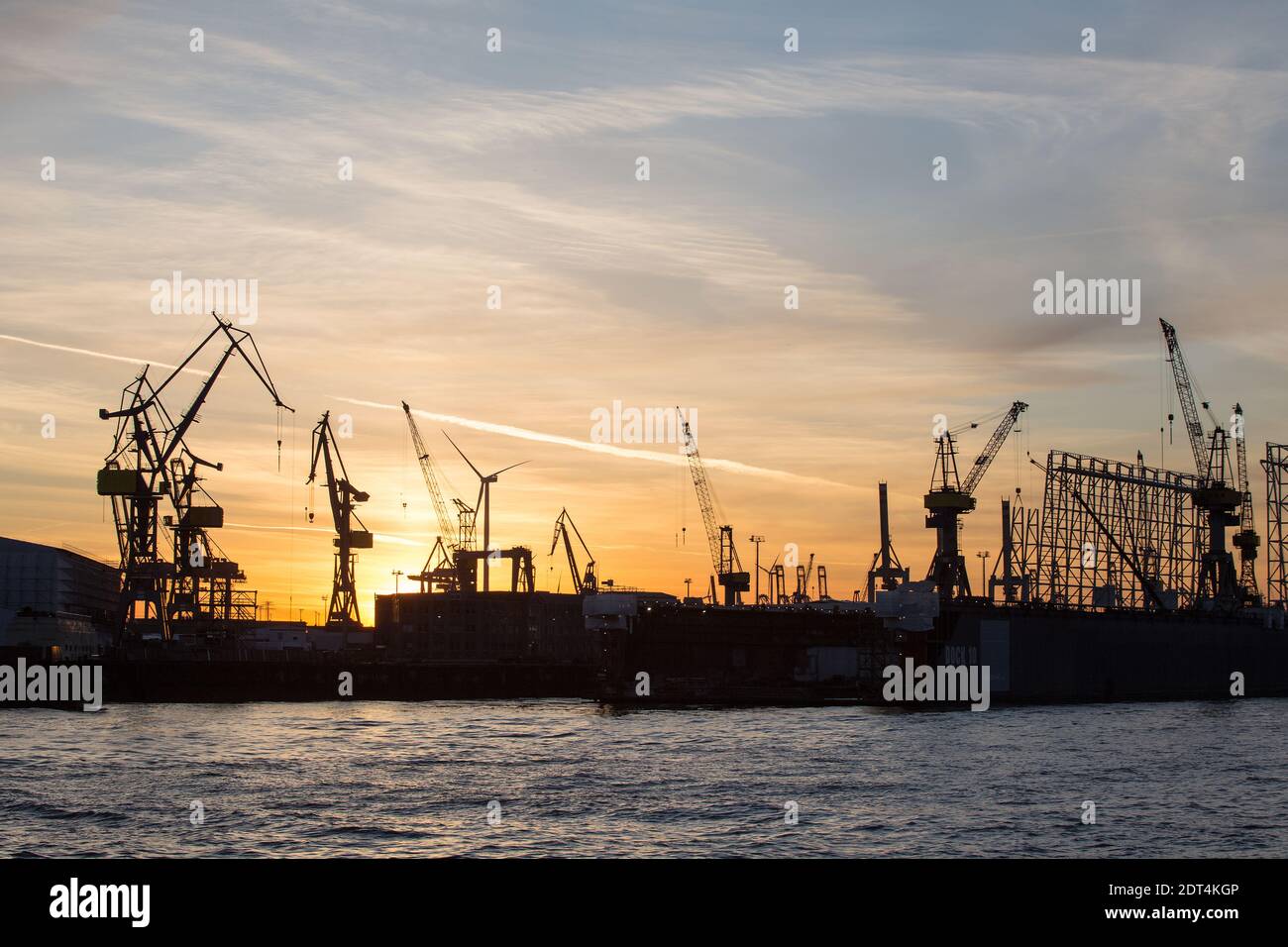 Die untergehende Sonne scheint hinter KrŠnen auf der Werft von Blohm + Voss, aufgenommen von der LandungsbrŸcken im Hamburger Hafen. Stock Photo