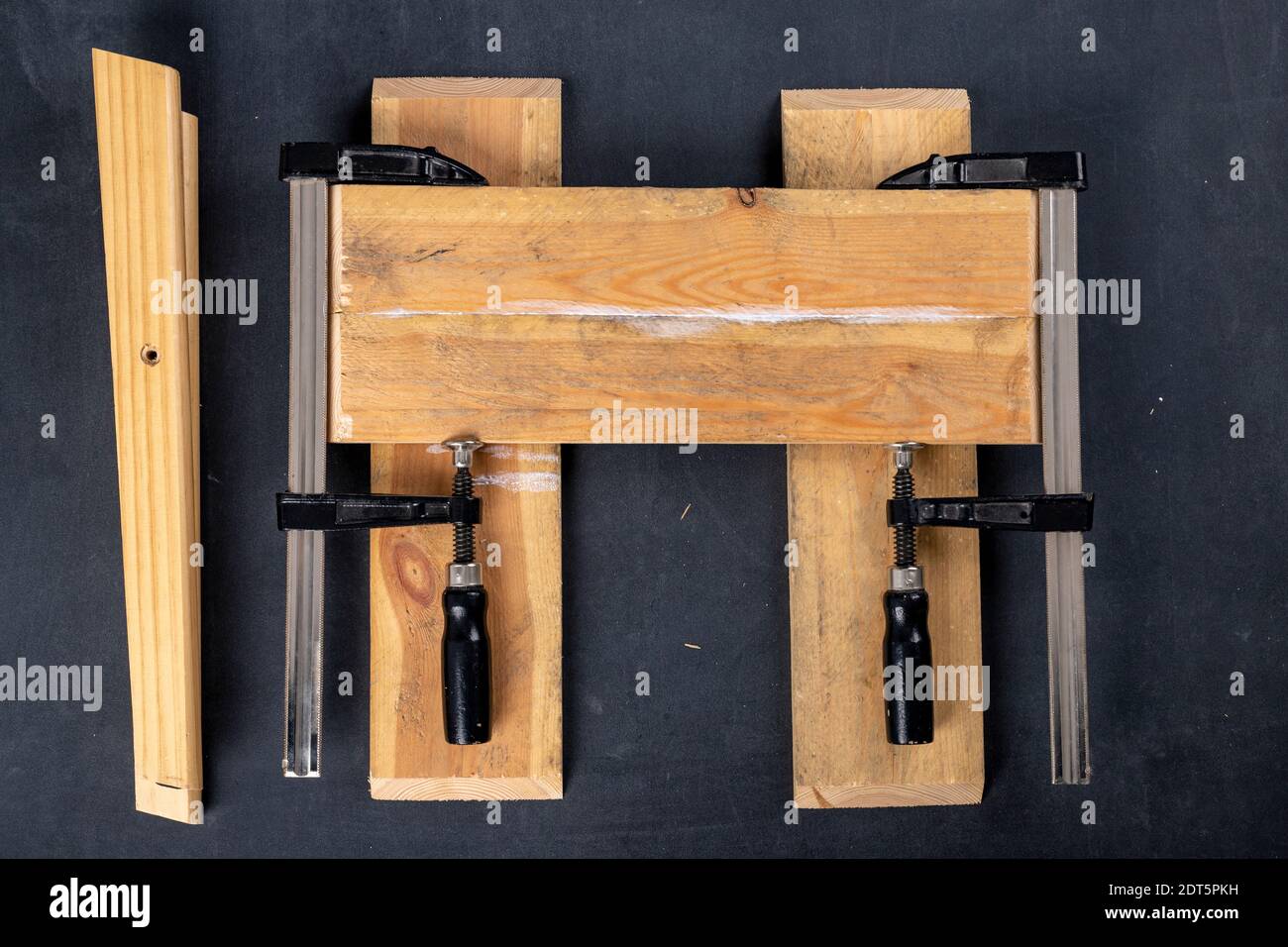 Gluing pieces of wood with carpentry glue. Boards in carpentry clamps. Dark background. Stock Photo