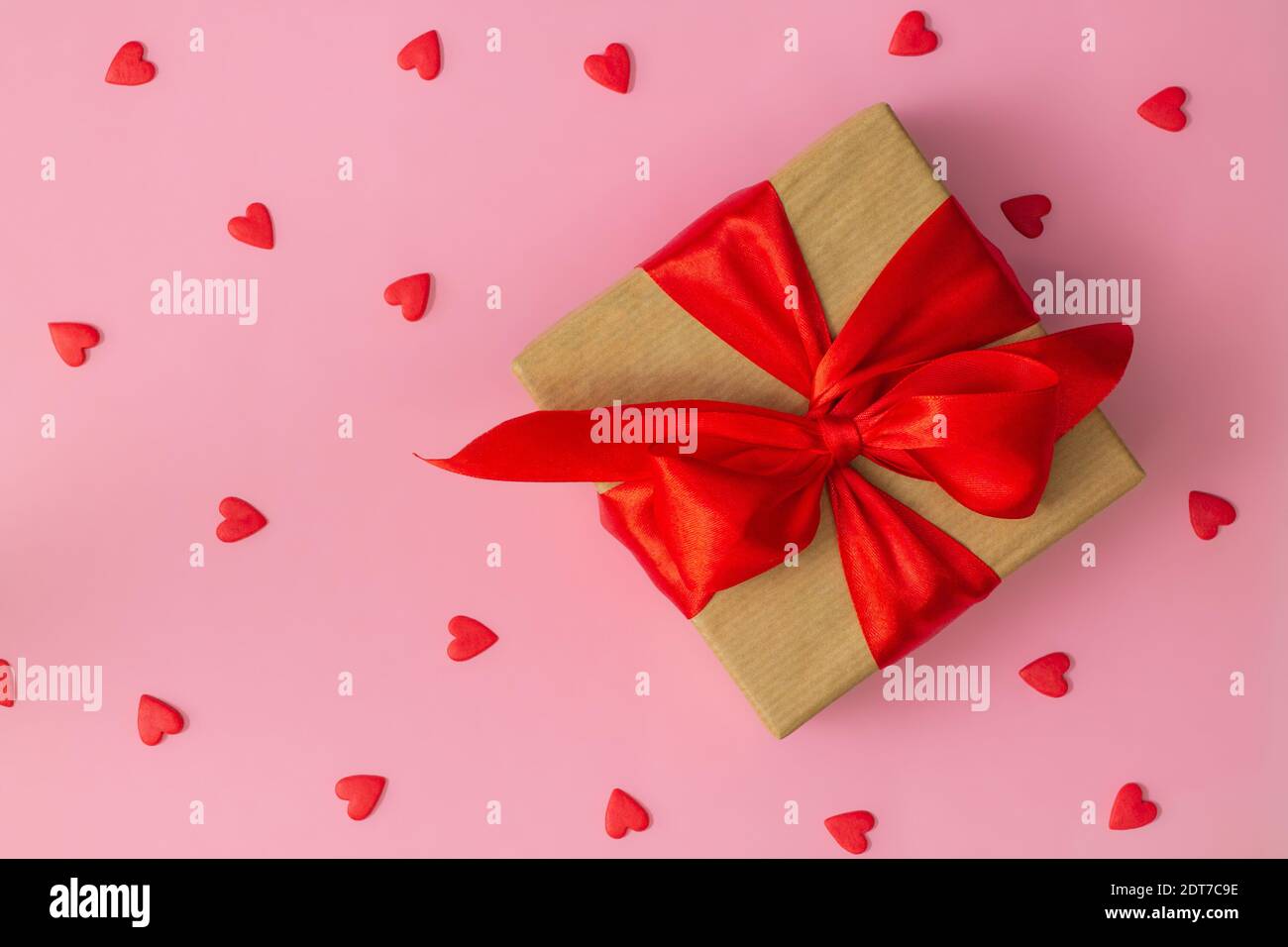 Gift wrapped in craft paper with red ribbon and bow and red hearts on ...