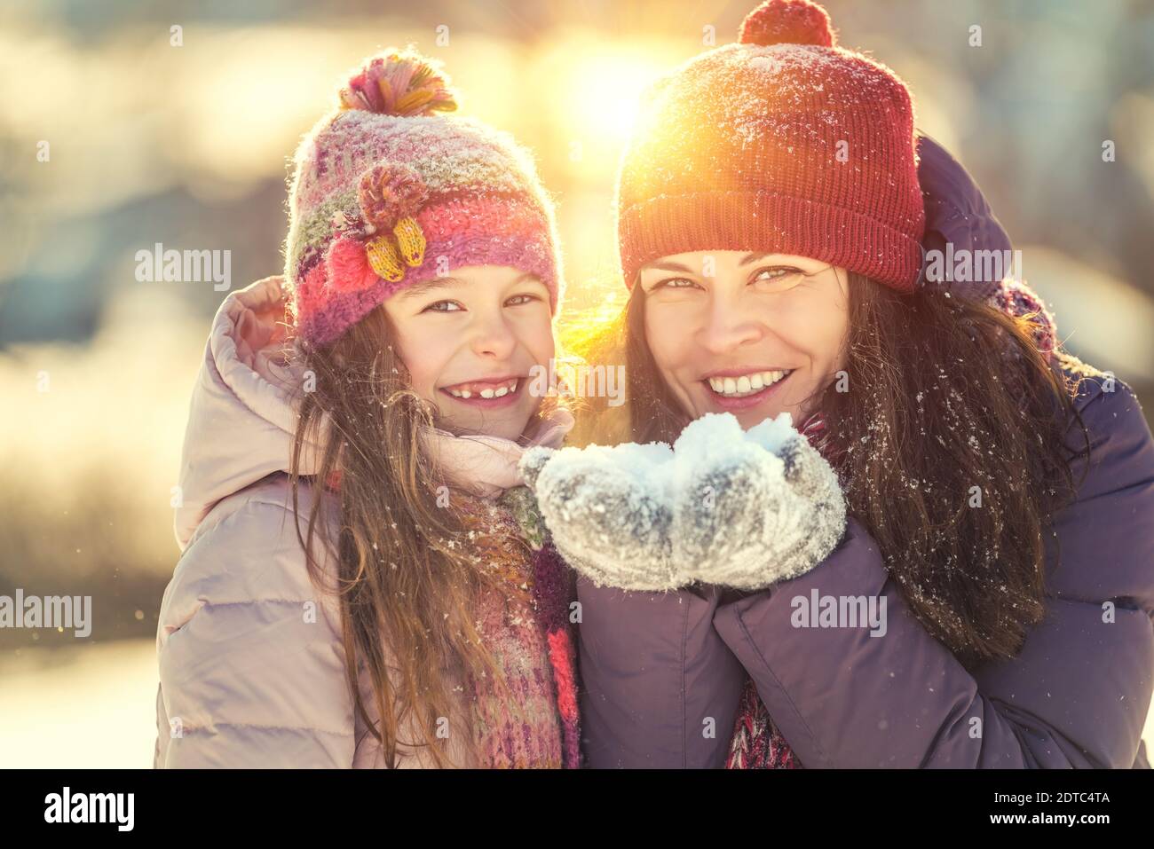 Little girl and her mother playing outdoors at sunny winter day. Active winter holydays concept. Stock Photo