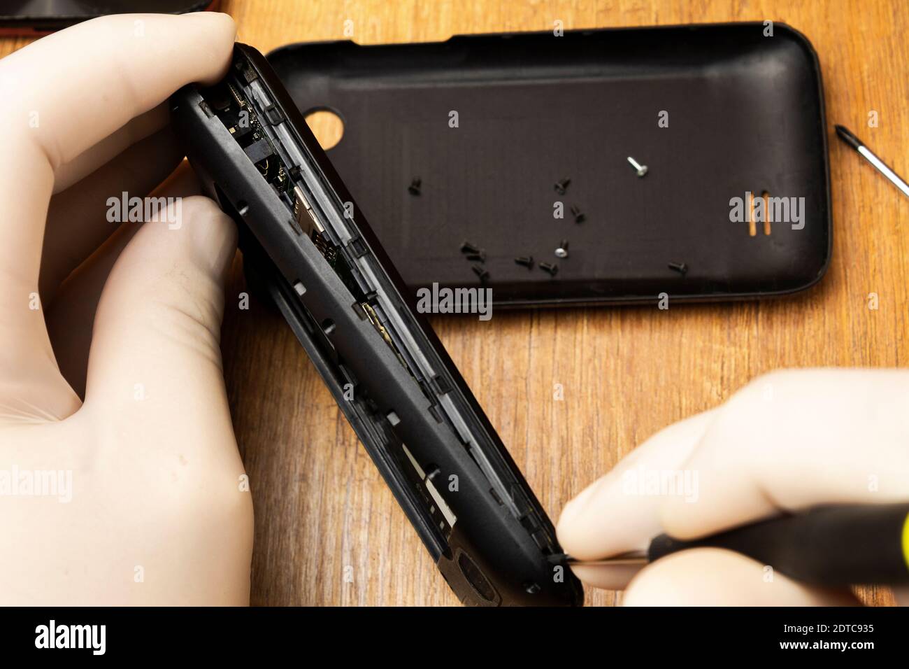 The master with a screwdriver disassembles a mobile phone on the table Stock Photo