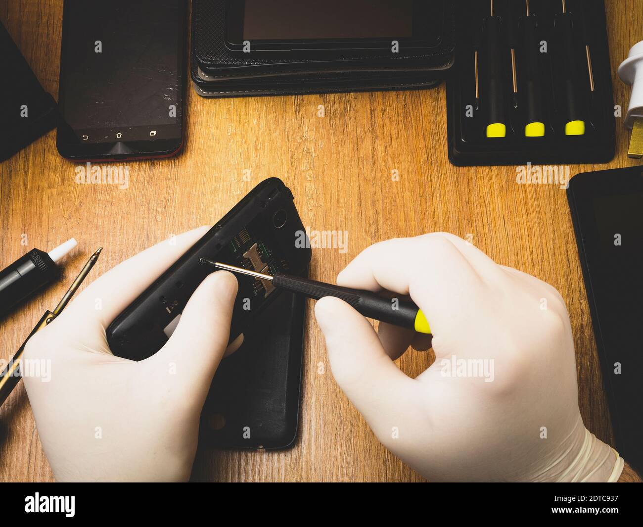 The master with a screwdriver disassembles a mobile phone on the table Stock Photo