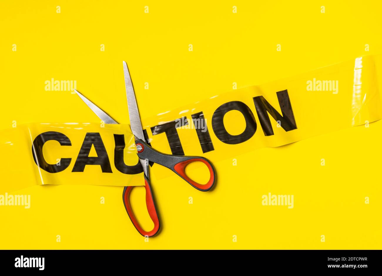 Studio shot of scissors cutting caution tape on yellow background Stock Photo