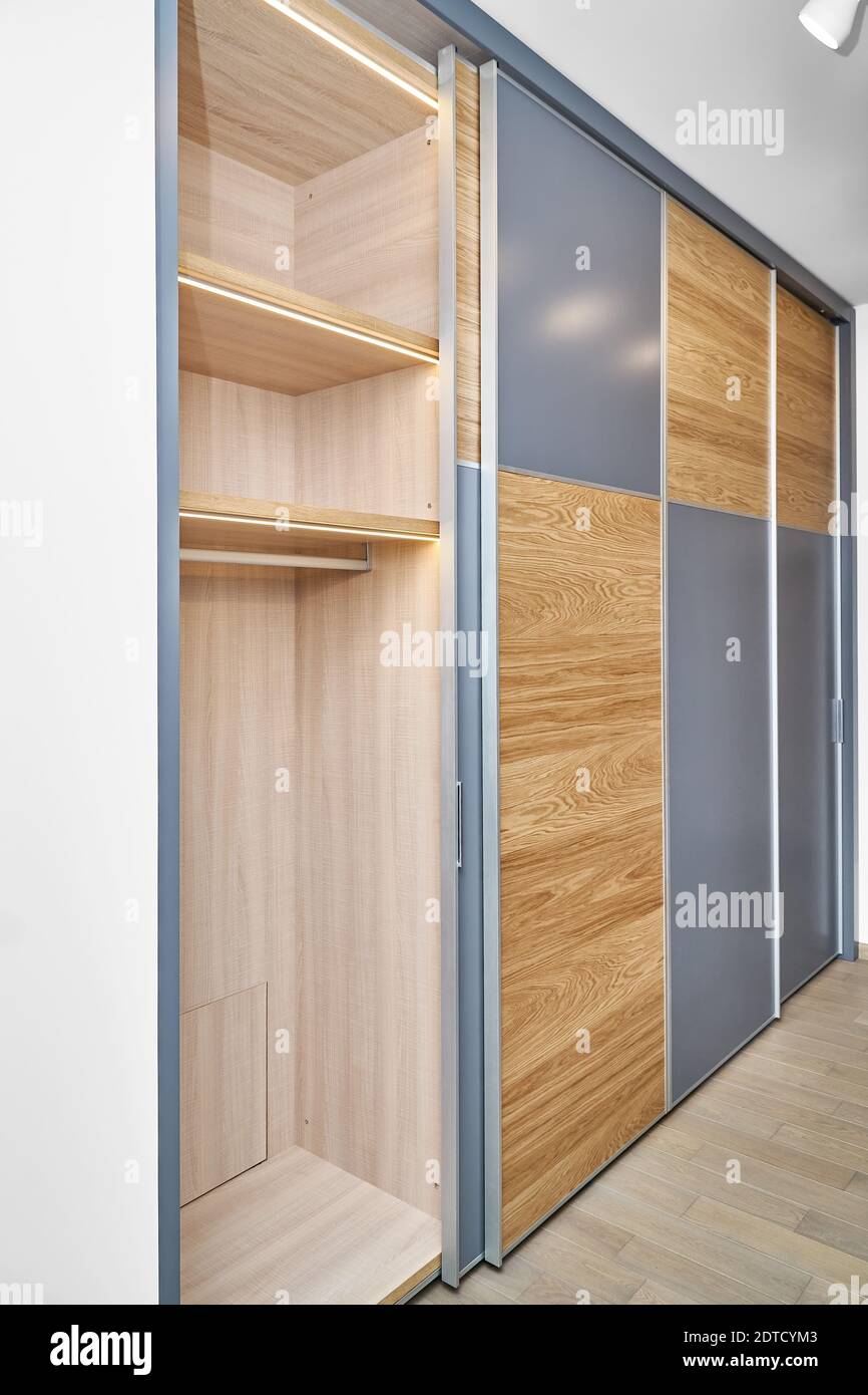 Stylish large wardrobe with LED lighting, sliding doors, shelves and inner drawer made of light laminated boards in contemporary interior designer lob Stock Photo