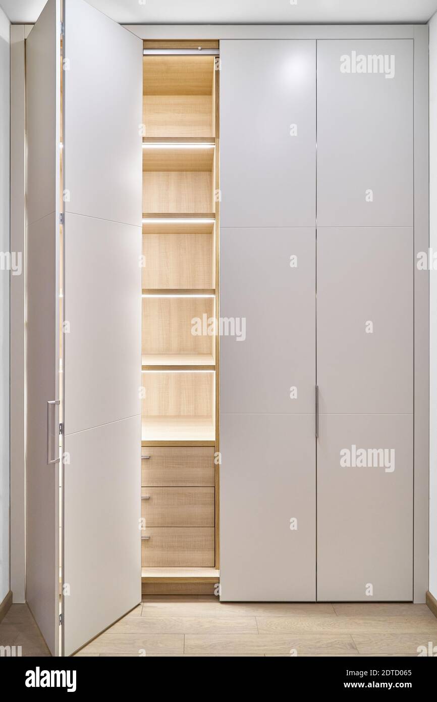 Large lobby wardrobe with LED lighting and white folding doors inner shelves and drawers made of light laminated boards in designed hallway Stock Photo
