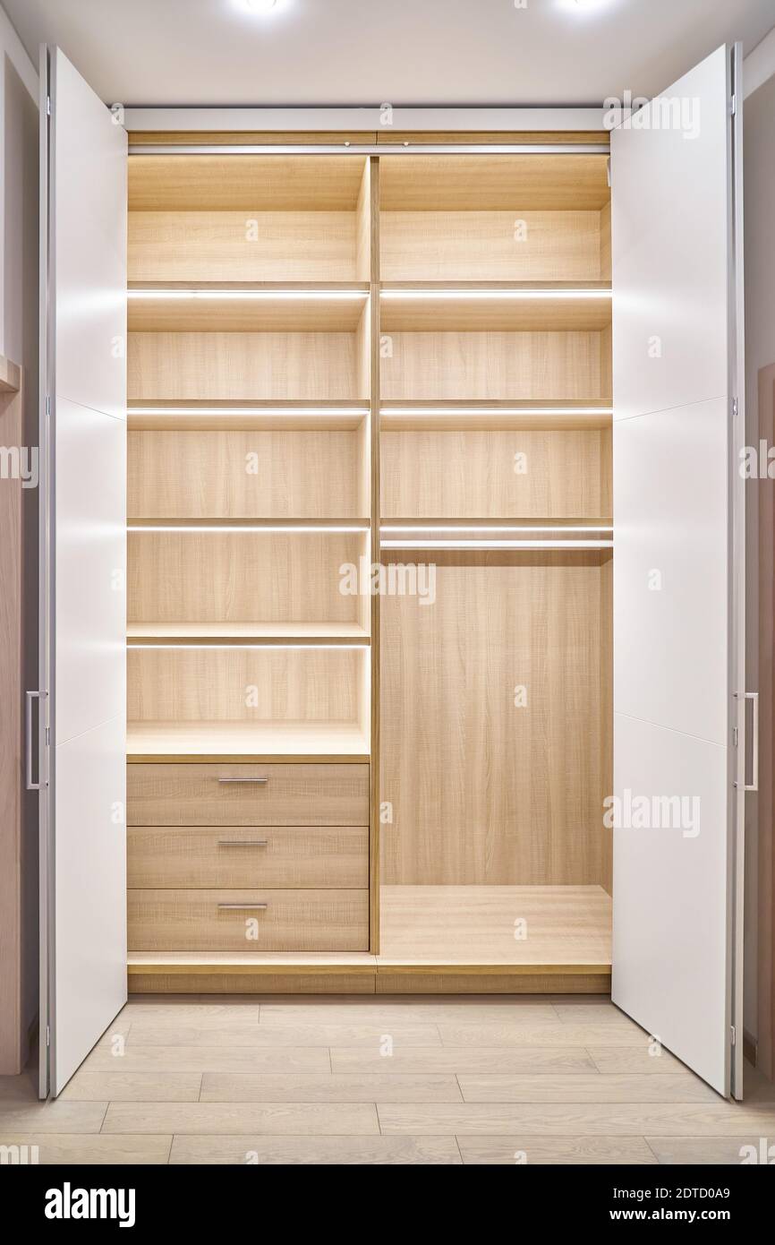 Large lobby wardrobe with LED lighting and white folding doors inner shelves and drawers made of light laminated boards in designed hallway Stock Photo