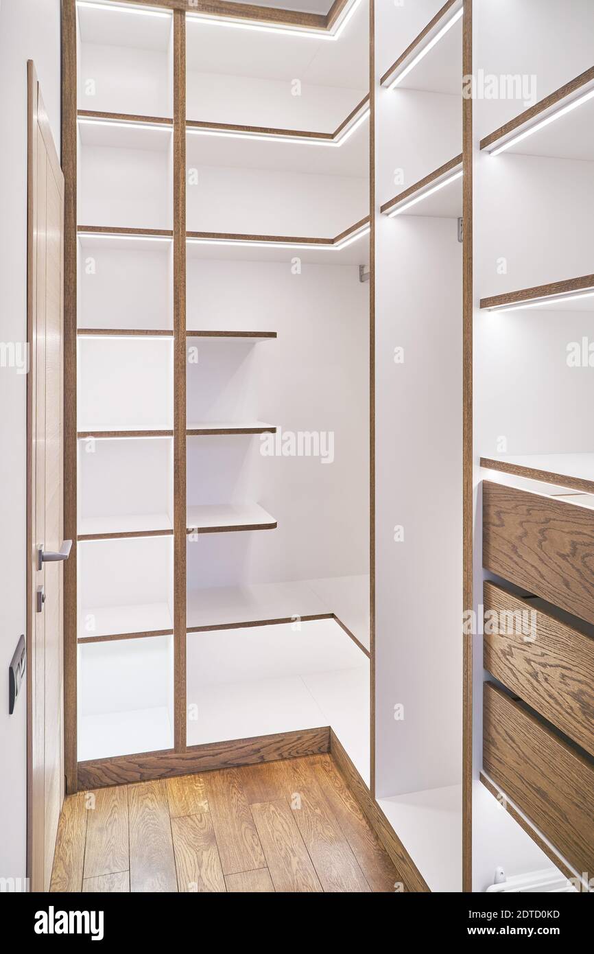 Elegant white shelving with LED lighting. Shelving of laminated boards with edges and faces of drawers made of oak veneer plywood sheets in walk-in cl Stock Photo