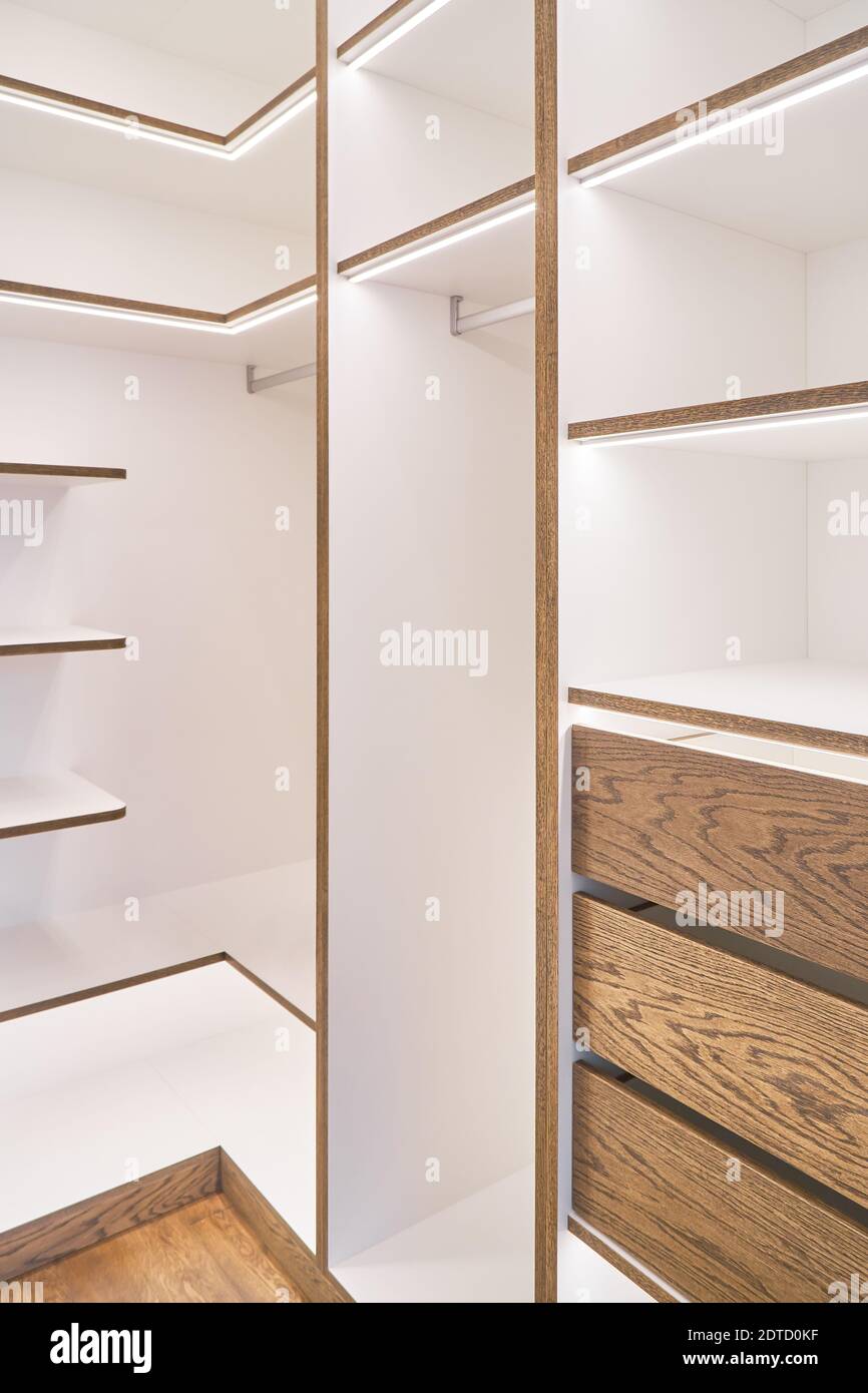 Elegant white shelving with LED lighting. Shelving of laminated boards with edges and faces of drawers made of oak veneer plywood sheets in walk-in cl Stock Photo