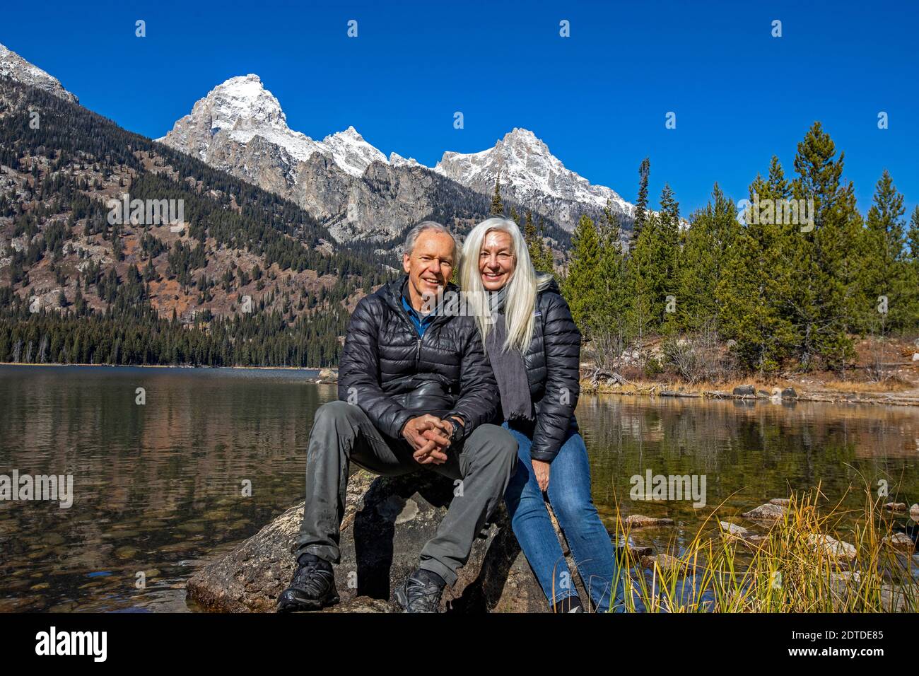 USA, Wyoming, Jackson, Grand Teton National Park, Outdoor portrait of senior couple sitting on rock by Taggart Lake in Grand Teton National Park Stock Photo