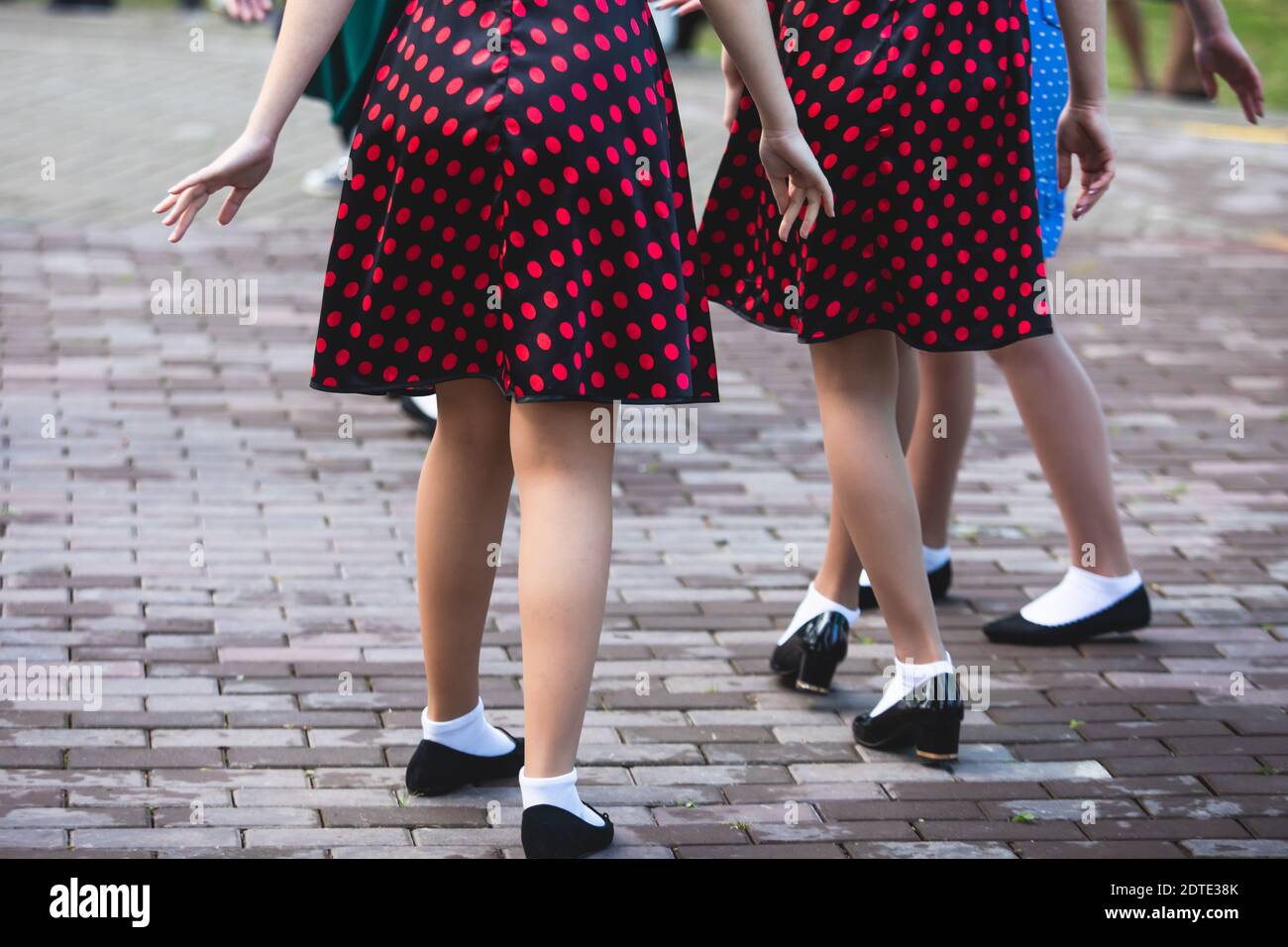 Young women wearing vintage polka dot dresses dancing in city park ...