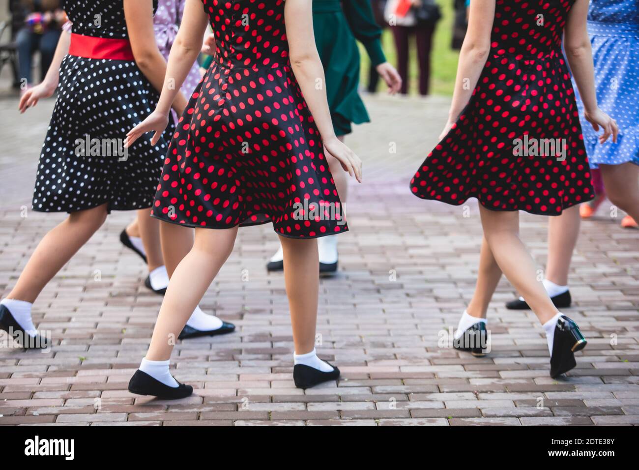 Young women wearing vintage polka dot dresses dancing in city park