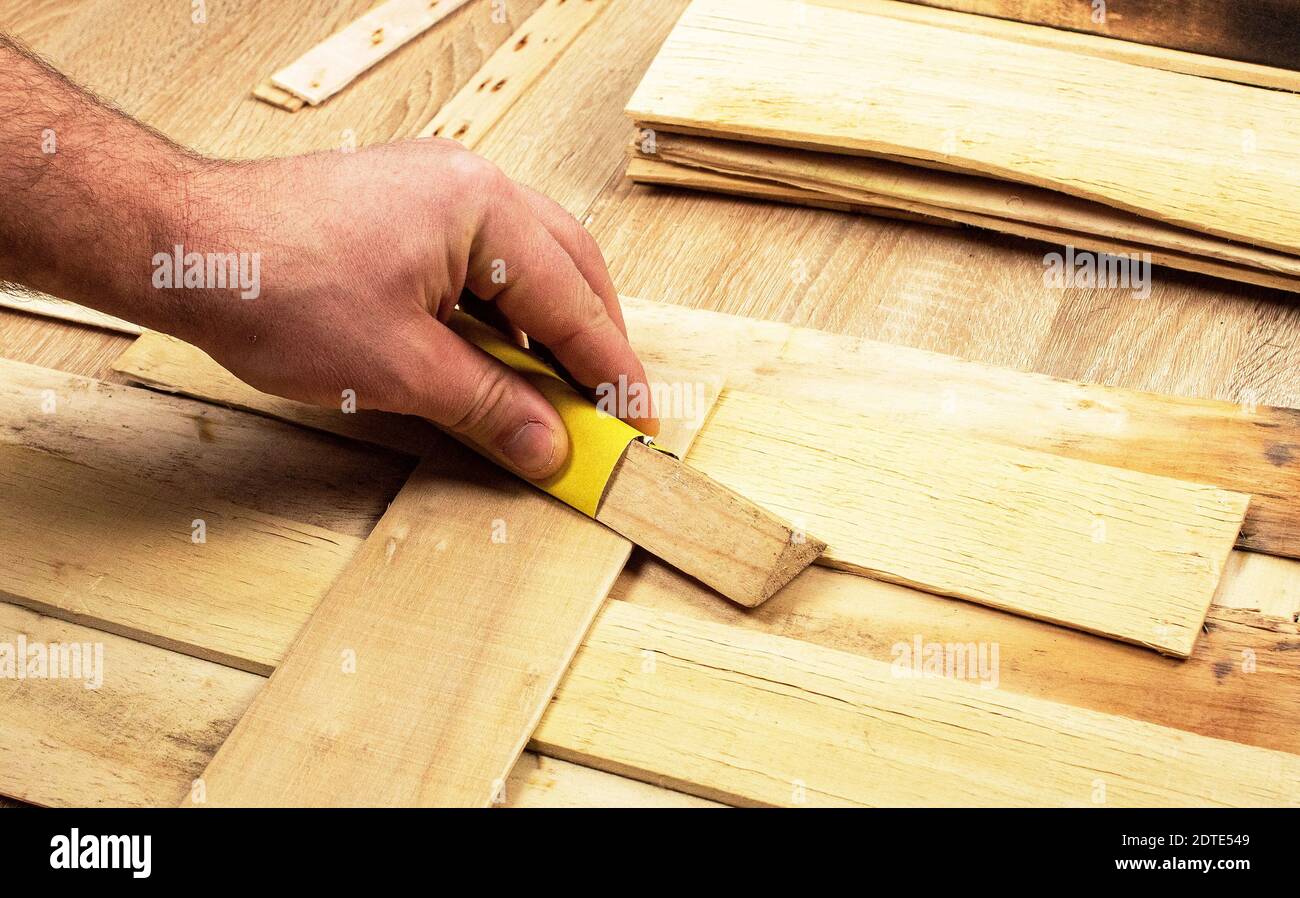Man hands processes the board with sandpaper. Sanding wooden boards