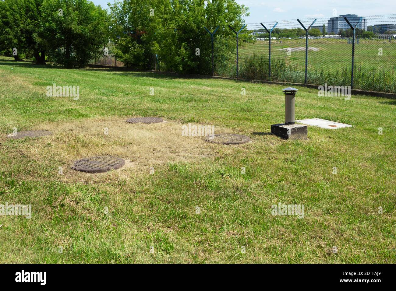 Metal sewer manholes on green grass. Four sewer hatches with an exhaust hood near the security facility. Large sewer well Stock Photo