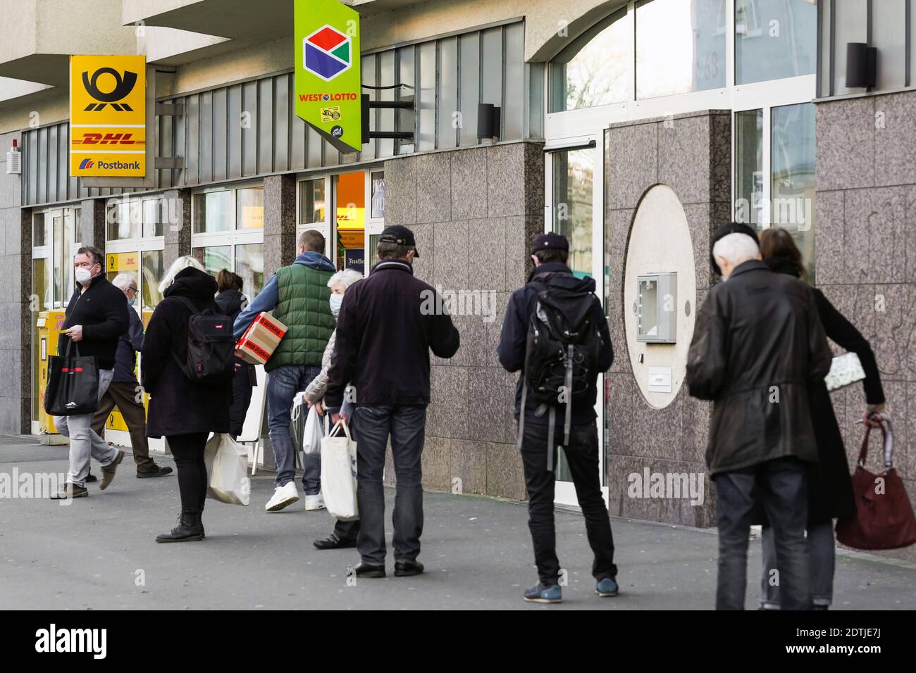 Dortmund, Germany, December 18th, 2020: Customers wait on the sidewalk in front of a branch of Deutsche Post / DHL in Dortmund. Due to the restrictions of the second lockdown of the corona pandemic, only 3 customers are allowed to stay in this branch at the same time. Stock Photo