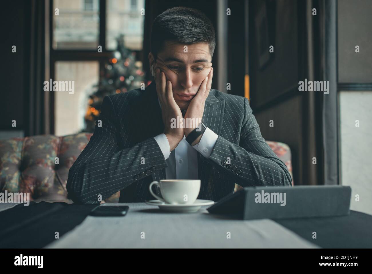 A young and attractive man uses his tablet while drinking coffe in an indoor restaurant Stock Photo