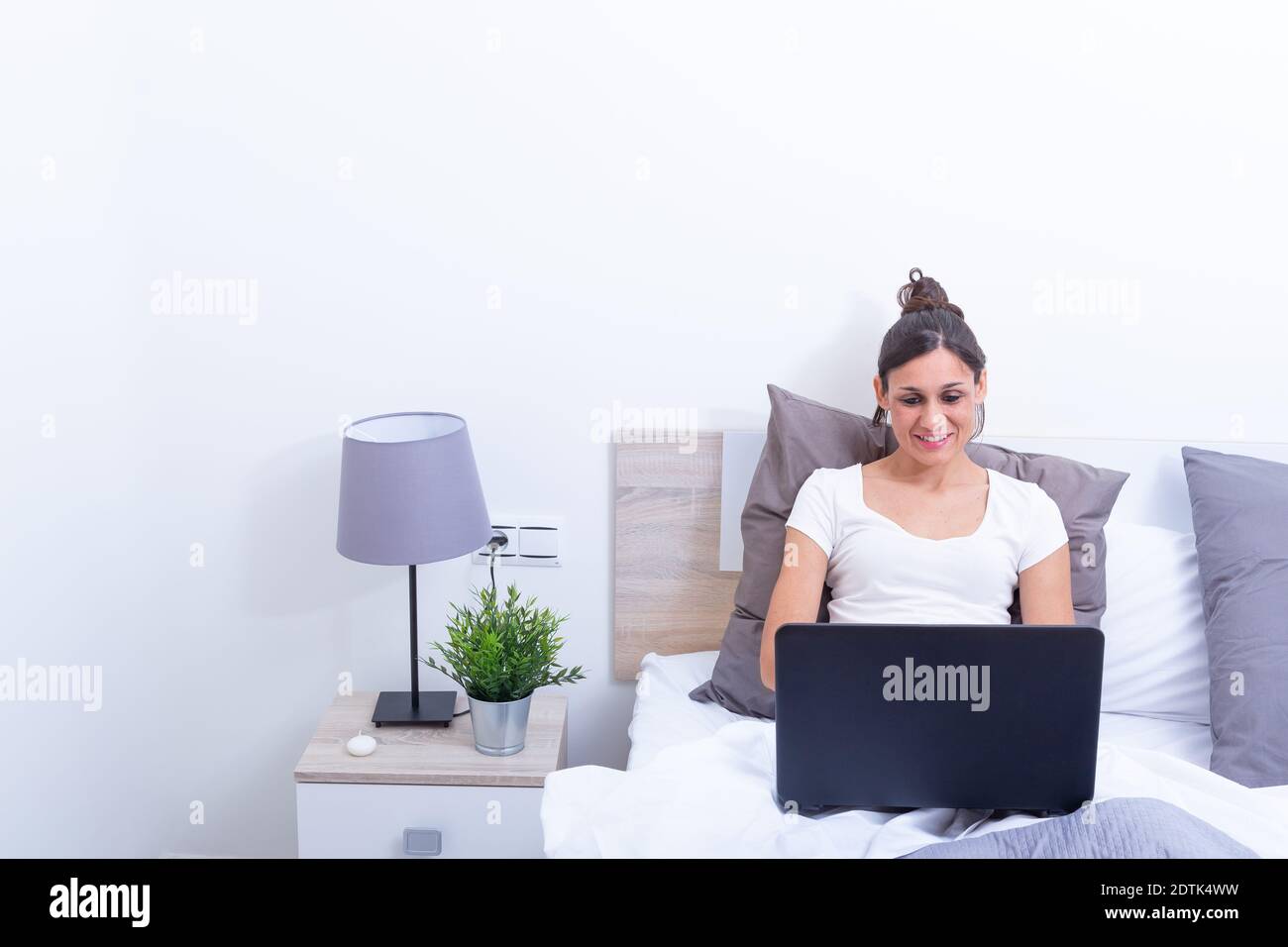 Happy smiling young woman,  relaxing in her bed with laptop computer. Stock Photo