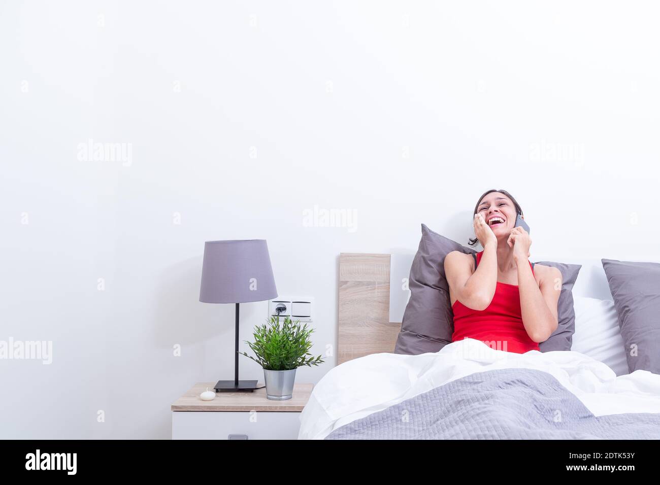 Happy young woman in bed laughing out loud while talking on the mobile phone Stock Photo