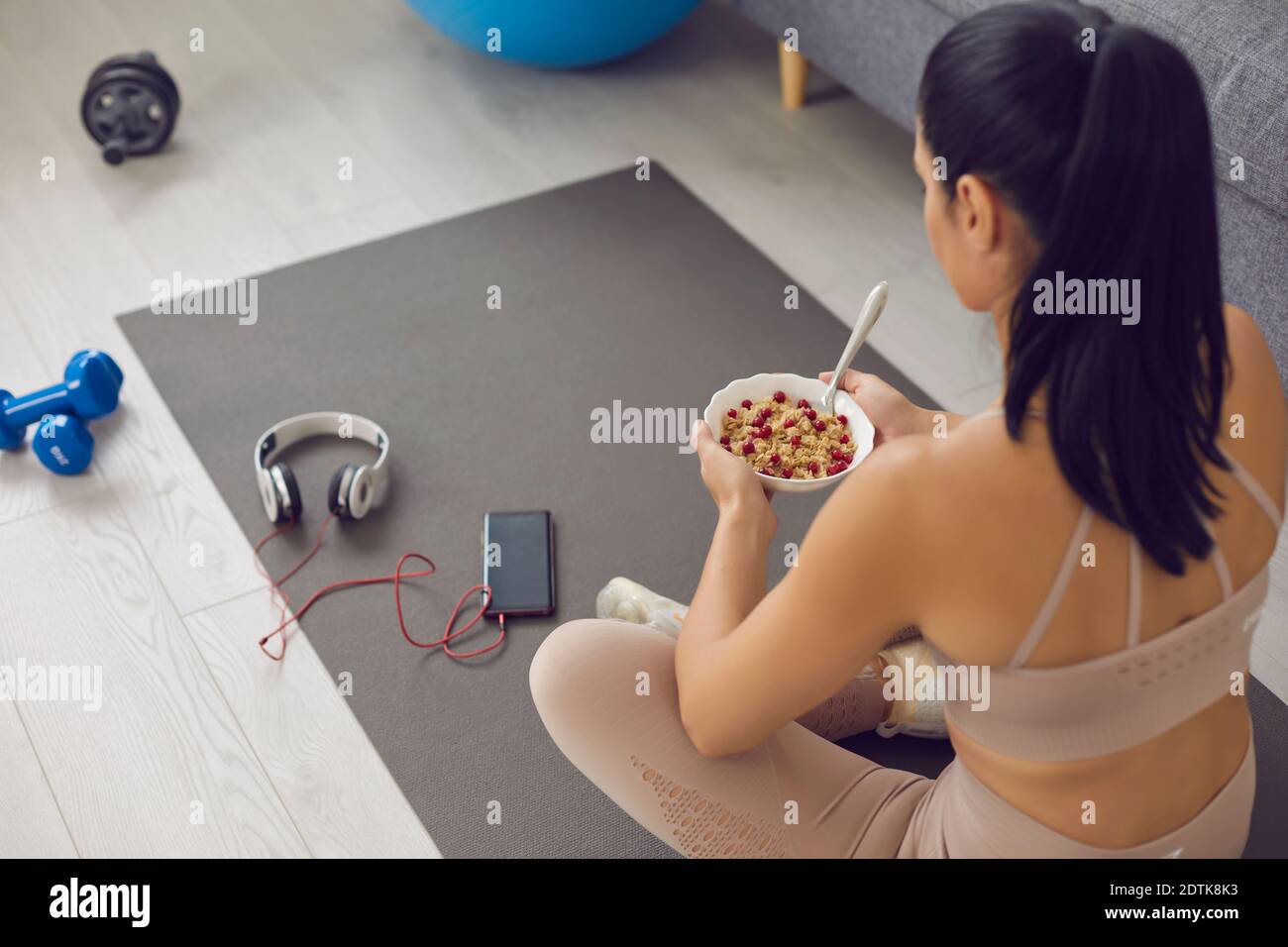 Woman relaxing on fitness mat and having healthy snack after sports workout at home Stock Photo