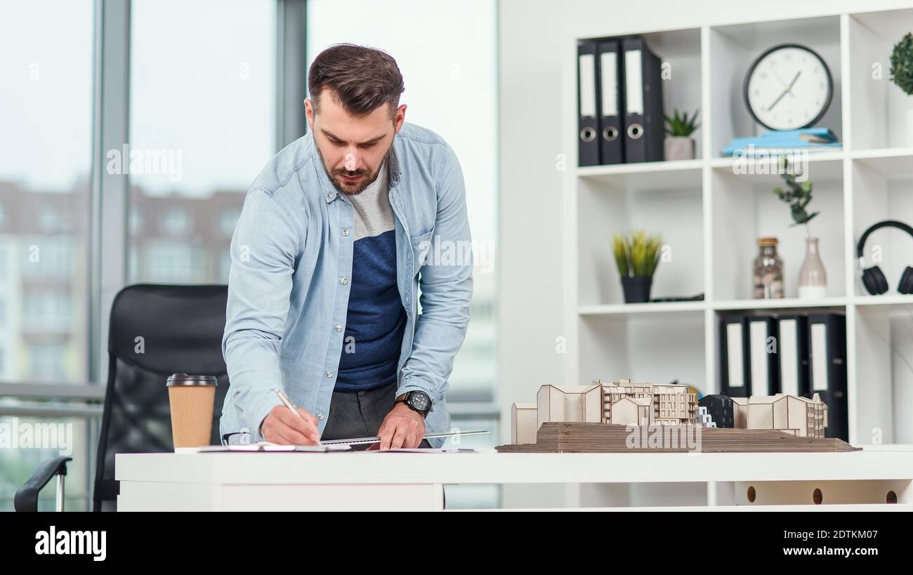 Handsome senior architect working on a construction project and examines the model on which he works. Stock Photo