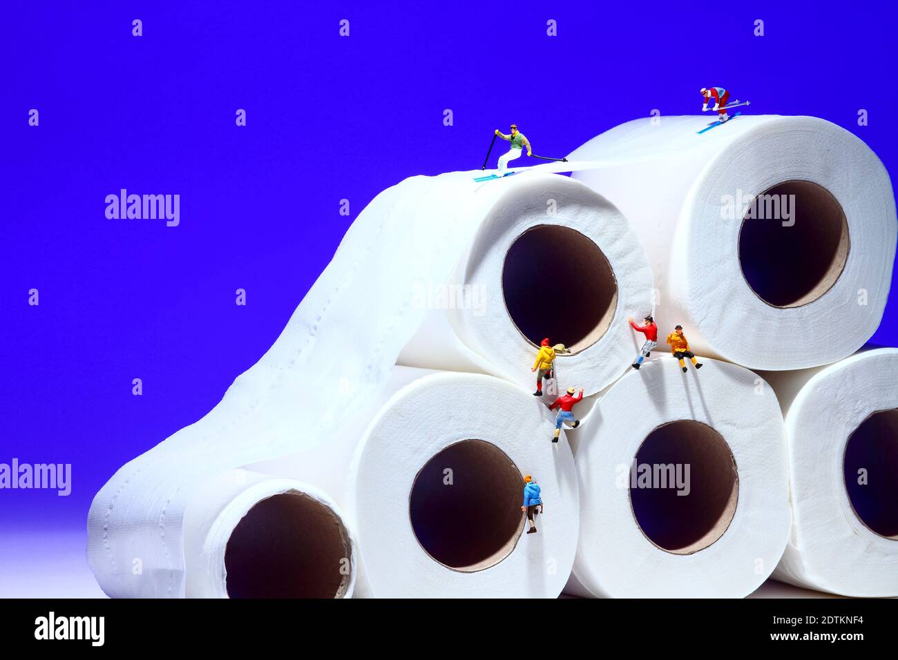 Conceptual image of miniature figure people skiing on toilet roll tissue whilst climbers scale the outside of the tubes Stock Photo