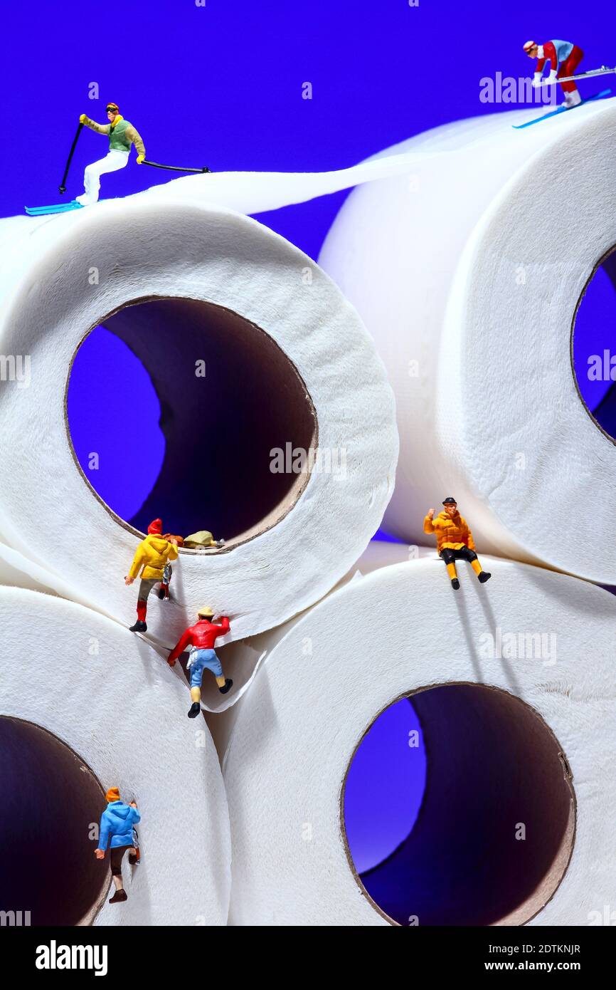 Conceptual image of miniature figure people skiing on toilet roll tissue whilst climbers scale the outside of the tubes Stock Photo