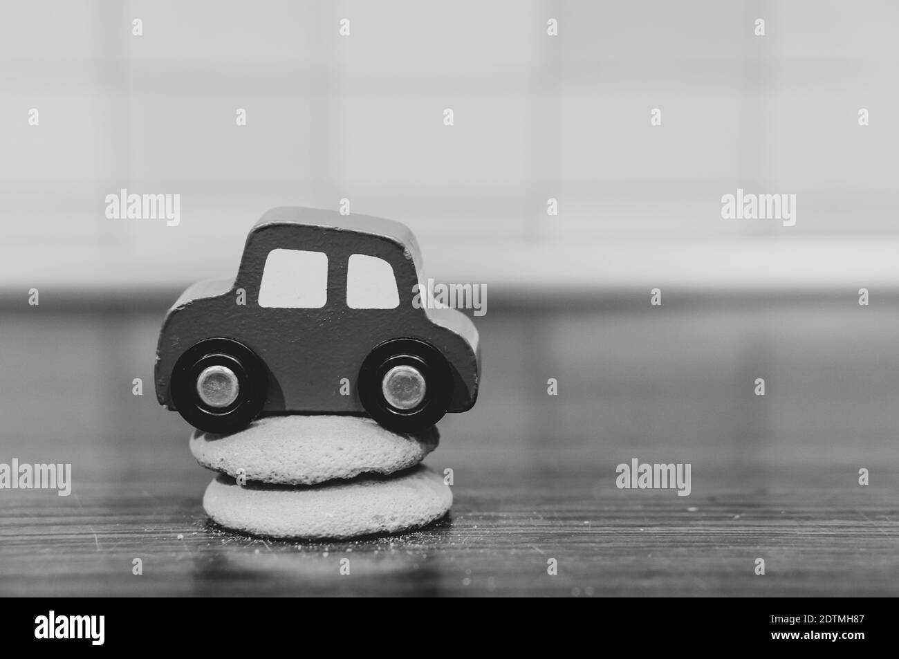 A grayscale shot of a wooden toy car on the cookies on the table Stock Photo