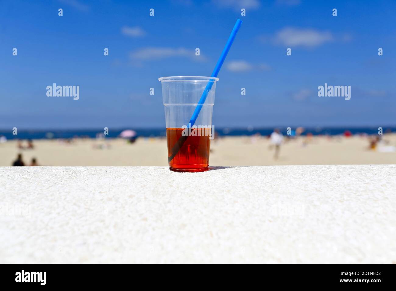 Arcachon (south-western France), on 2019/07/07. Glass of water and grenadine with a blue straw on the low wall by the beach of Thiers, and blue sky in Stock Photo