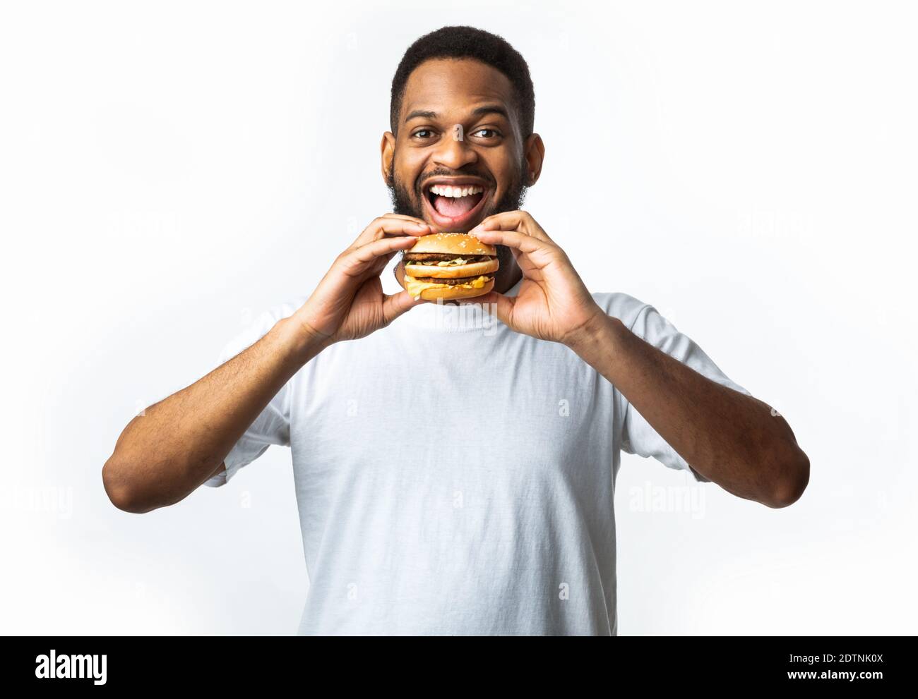 African Guy Biting Burger Eating Unhealthy Junk Food, White Background Stock Photo