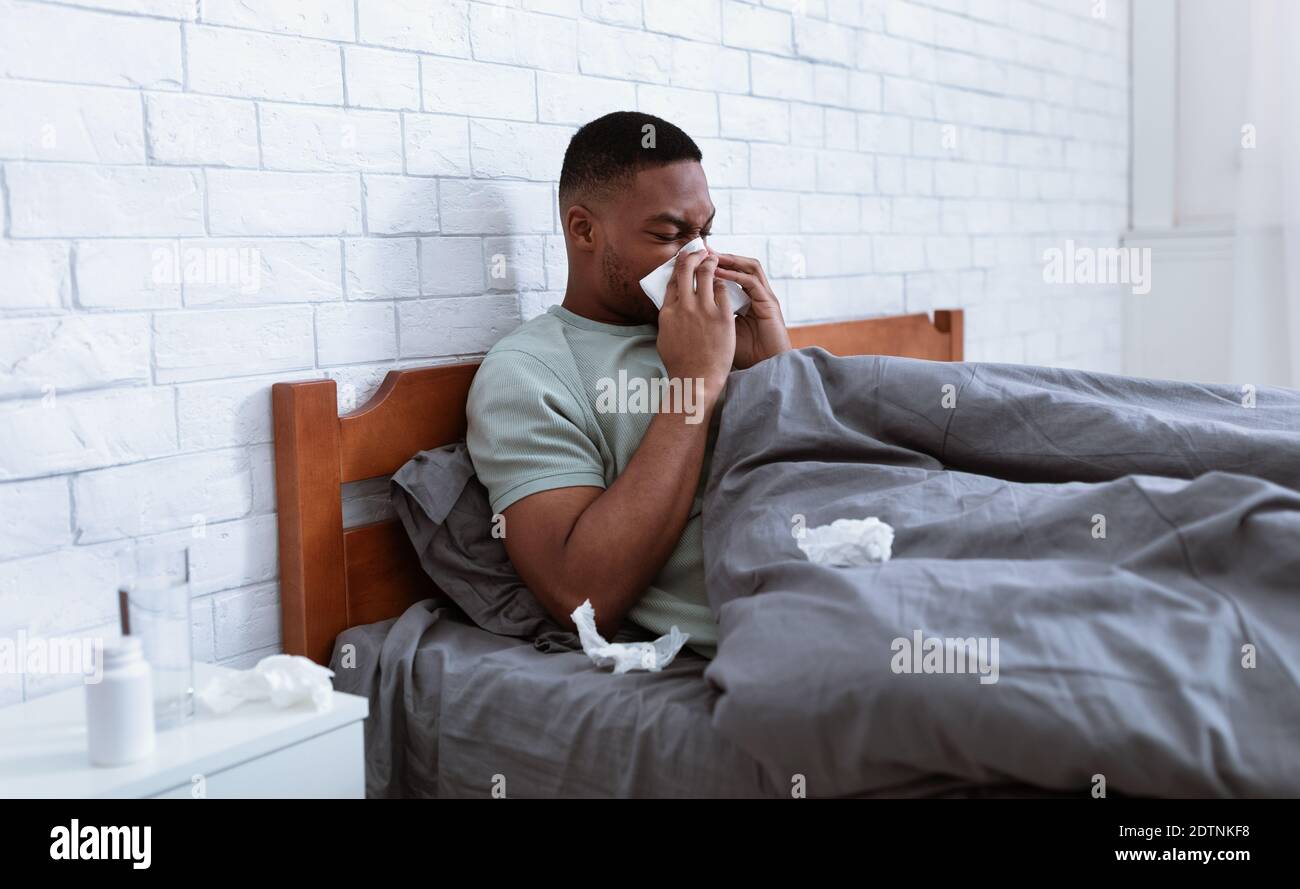 Sick Man Blowing Nose In Tissue Lying In Bed Indoor Stock Photo