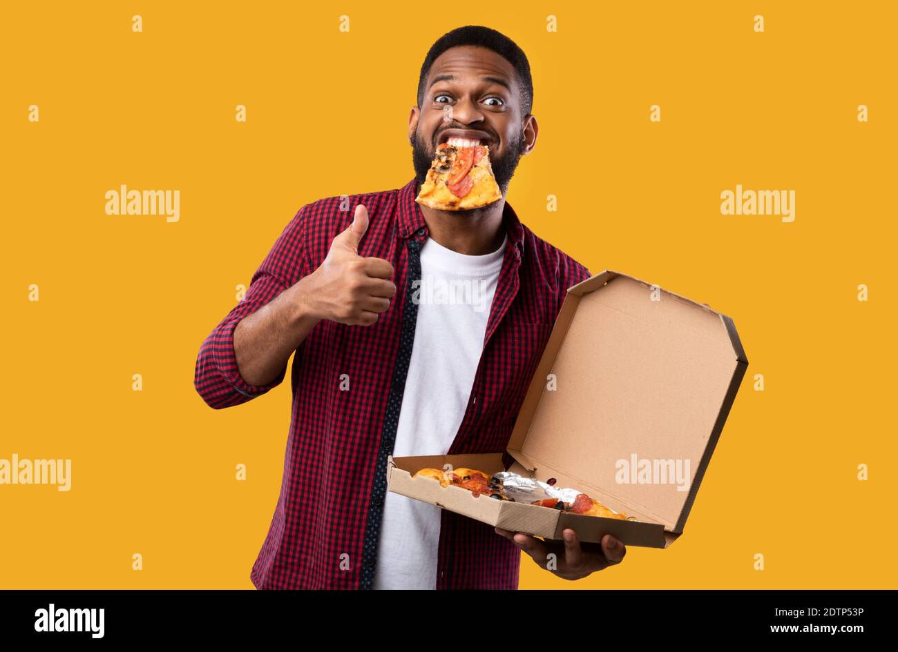 Black Guy With Pizza In Mouth Gesturing Thumbs Up Yellow Background 