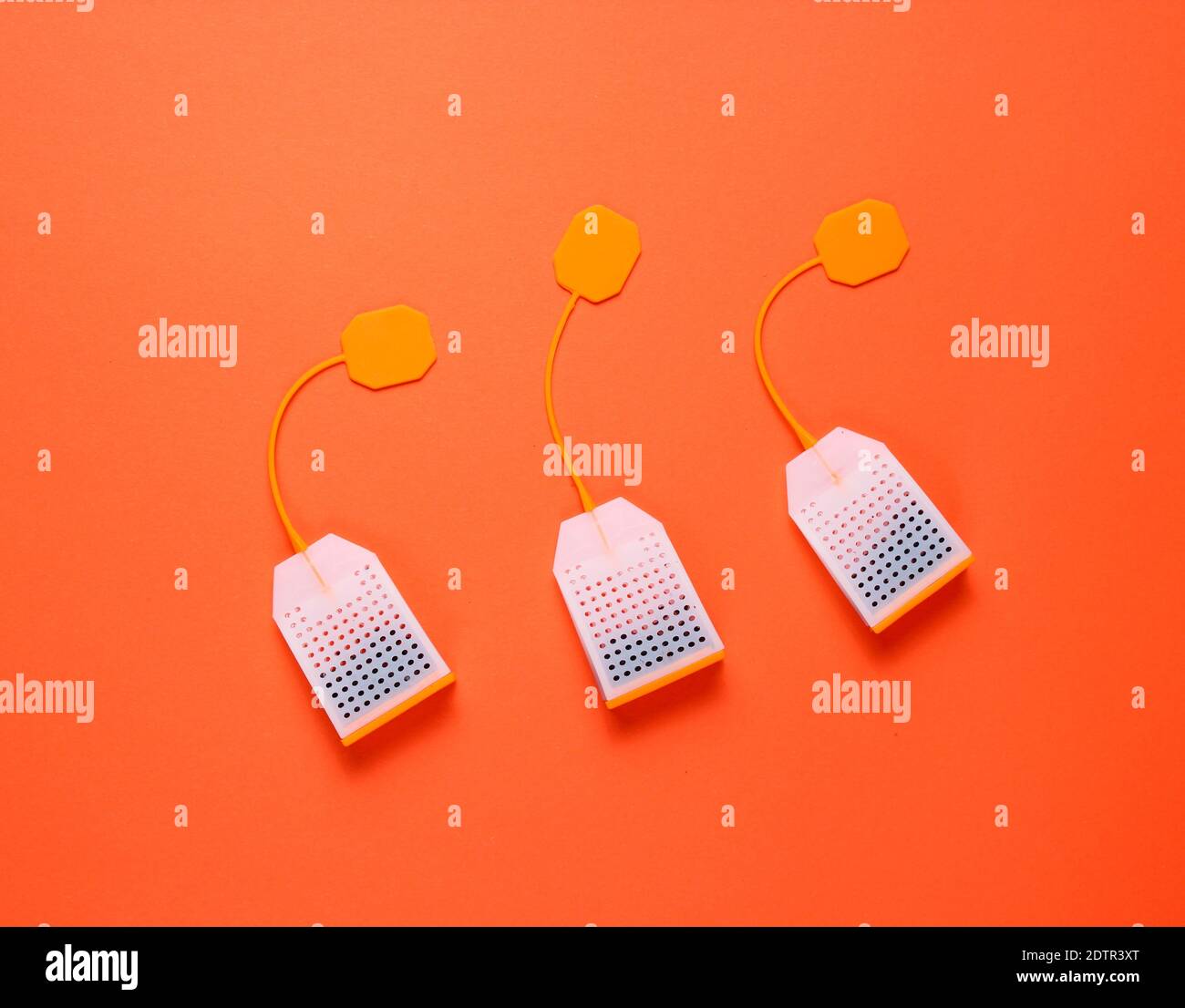Three silicone tea bags on orange background. Top view, minimalism