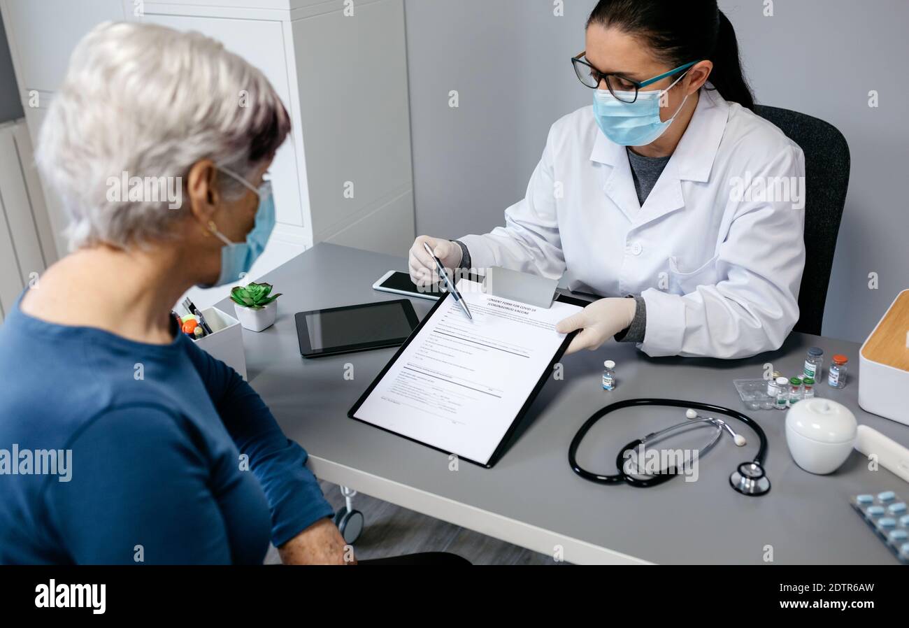 Female doctor explaining to her patient the consent form to coronavirus vaccine Stock Photo