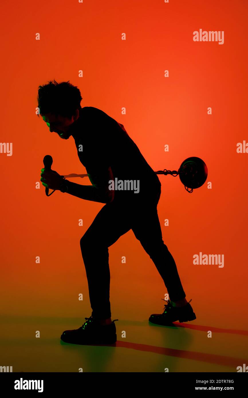 Expressive. Silhouette of young male guitarist isolated on orange gradient studio background in neon. Beautiful shadow in action, performing. Concept of human emotions, expression, ad, music, art. Stock Photo