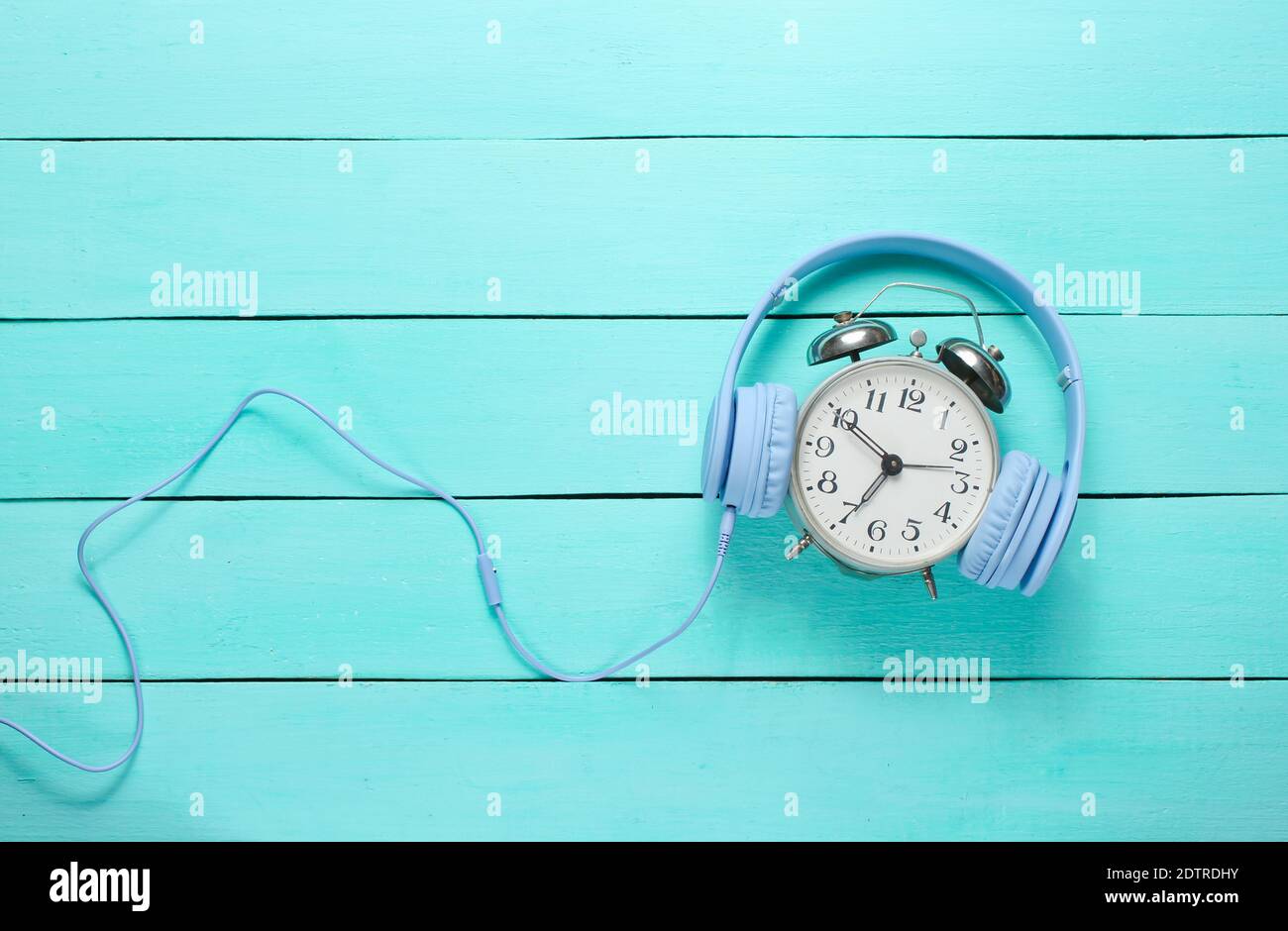 Vintage alarm clock with headphones on wooden background. Top view